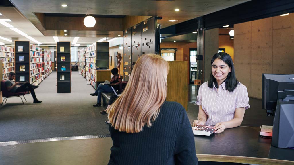 Student smiling as she checks out book at service desk in library
