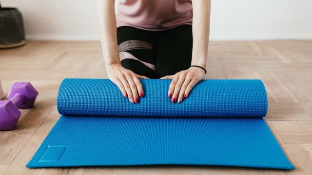 Woman rolling out yoga mat at home