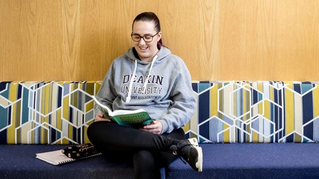 Smiling female student reading book on campus