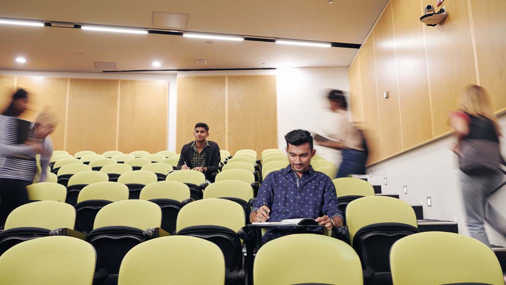 Student working in lecture theatre with other students moving in background