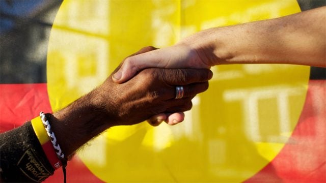 Hands clasped in front of Aboriginal flag