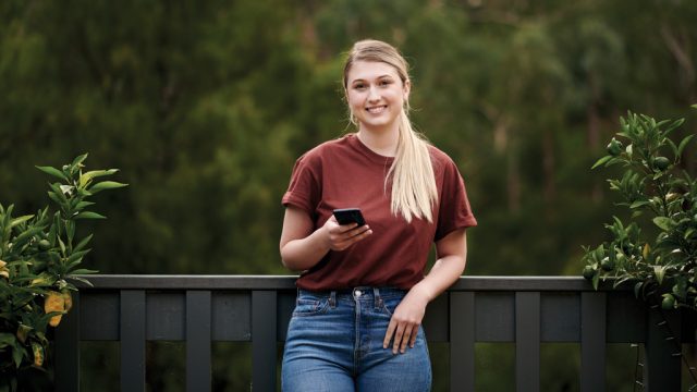 Student smiling as she looks at mobile phone outside at home