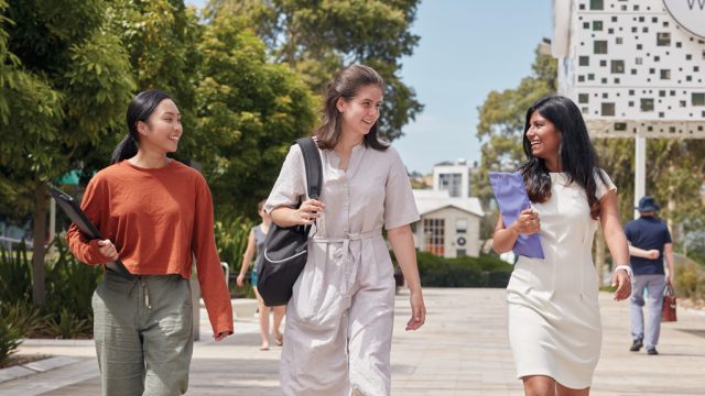 Three students chatting as they walk along Morgan's Walk at Burwood Campus