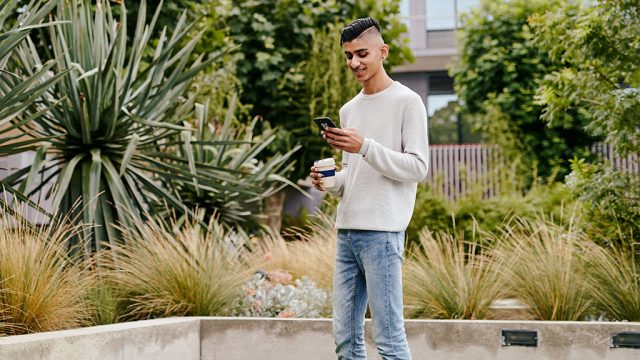 Male student outside at Waurn Ponds with coffee cup and phone