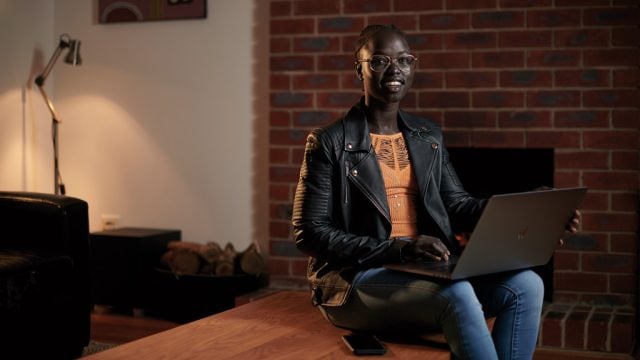 Student smiling as she studies on laptop in living room at home