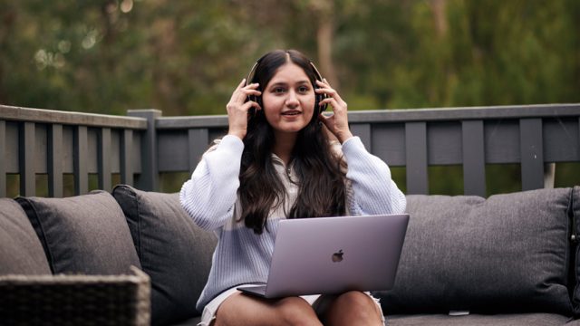 Student placing on headphones while working on laptop outside