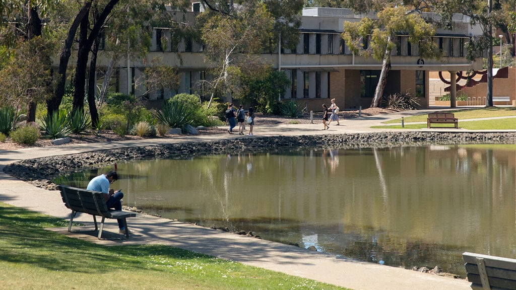 Student sitting on bench near pond at Waurn Ponds Campus