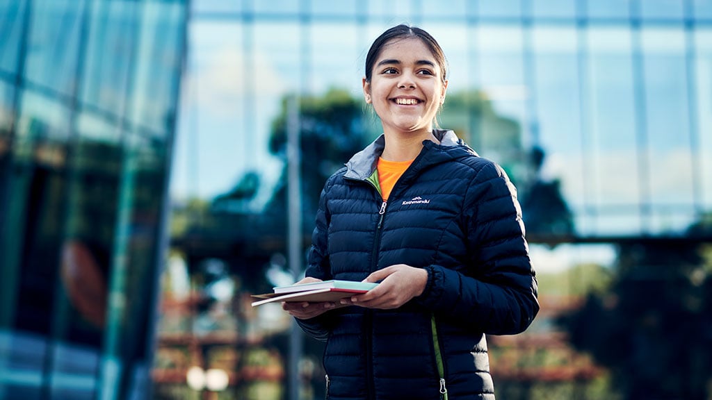 Smiling female student holding books outside Burwood building