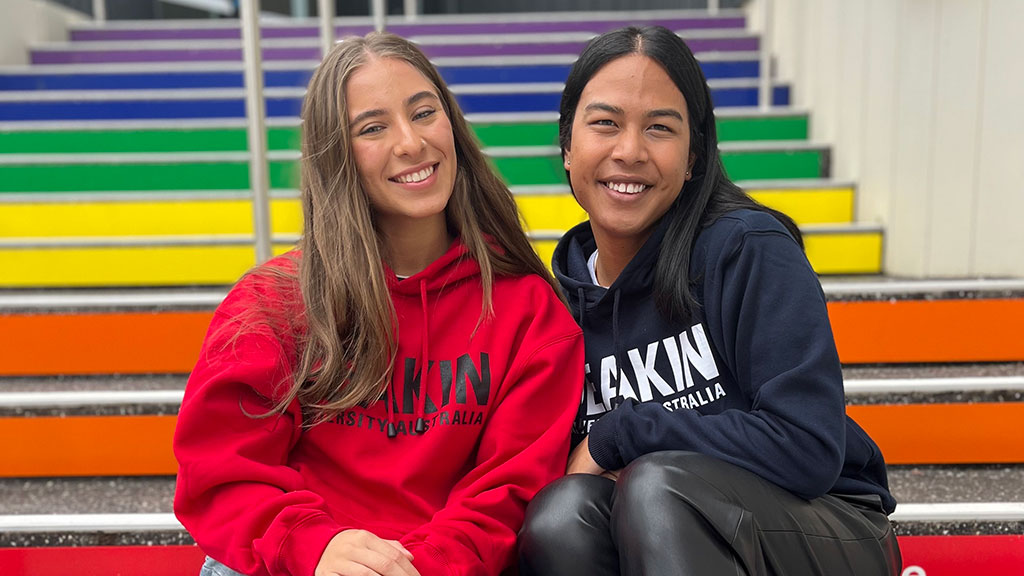 Two Deakin students wearing Deakin-branded hoodies sitting on stairs at Waurn Ponds Campus
