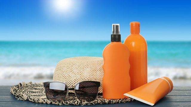Sunscreen, hat and sunglasses in front of beach scene