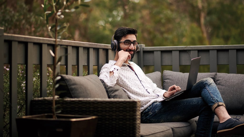 Student smiling as he works on laptop outside at home
