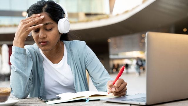 Female student looking stressed with laptop and study materials