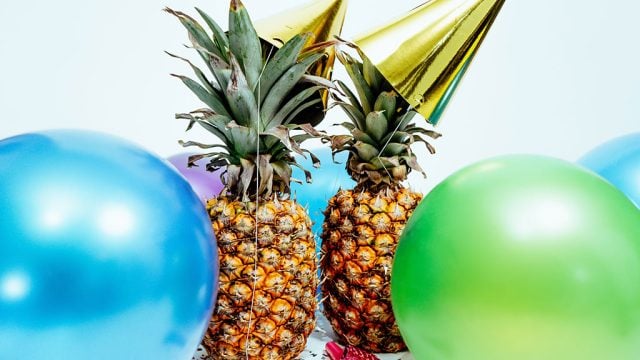 Two pineapples with party hats and balloons