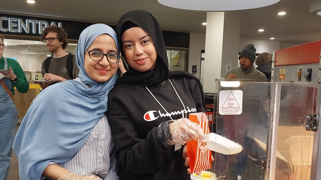 Two students scooping popcorn into a bag.