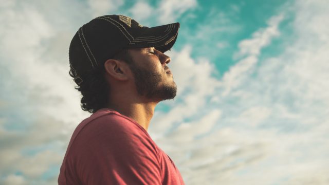 Man relaxes with eyes closed against sky backdrop