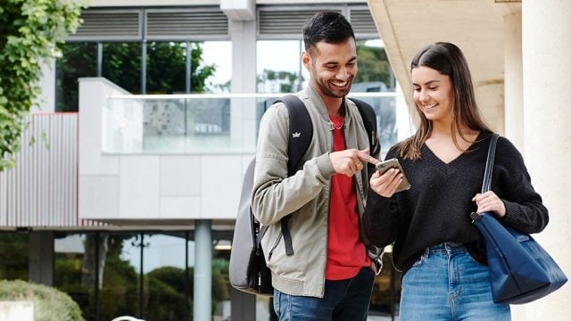 Male and female student looking at phone on campus