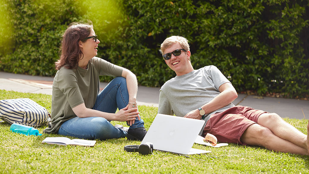 Male and female student sitting on grass with study materials