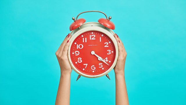 Hands holding up an alarm clock on a bright blue background