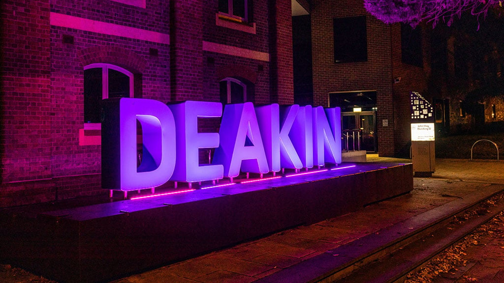 Deakin sign at Waterfront Campus lit up in purple