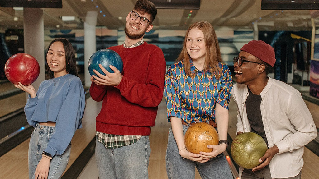 Four young adults holding bowling balls in tenpin alley