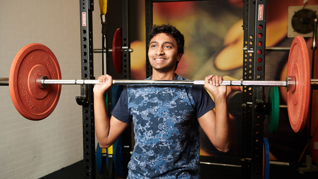 Student smiling as he lifts weights at DeakinACTIVE Burwood gym