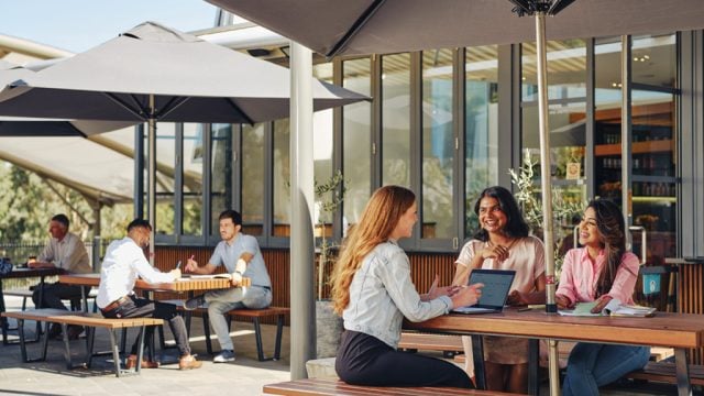Three students chatting in outdoor dining area at Burwood Campus