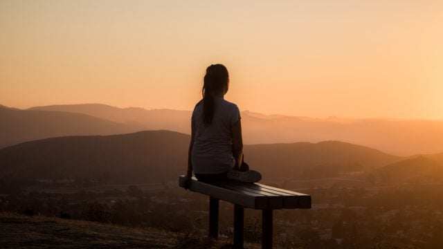 Woman sitting on bench watching sunset