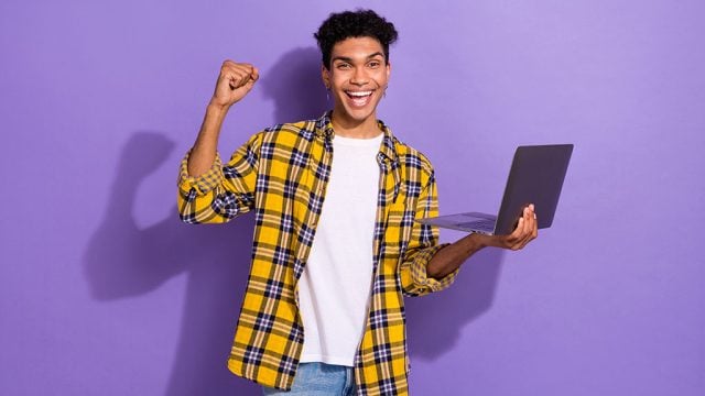 Smiling young man holding lap top and doing a fist pump