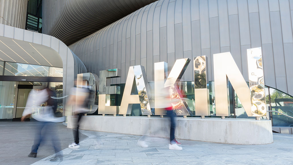 Blurred image of people walking past Deakin sign on Burwood Campus