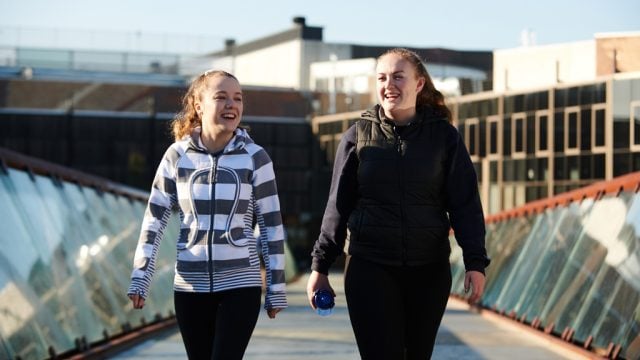 Two students smiling and chatting as they walk across the footbridge at Burwood Campus