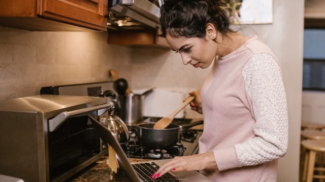 Woman looking at laptop while cooking in kitchen