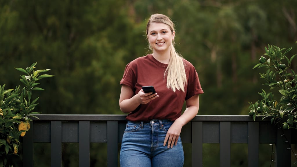 Student smiling and holding phone in outdoor area