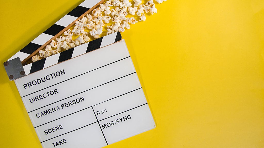 Movie clapper and popcorn on yellow background