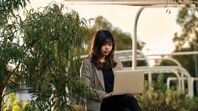 A student sitting in a campus garden using a laptop