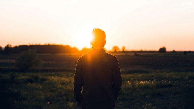 Man standing in field with sun setting behind him