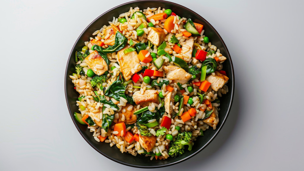 Bowl of brown fried rice with chicken, broccoli, spinach, carrot, capsicum, peas and zucchini.