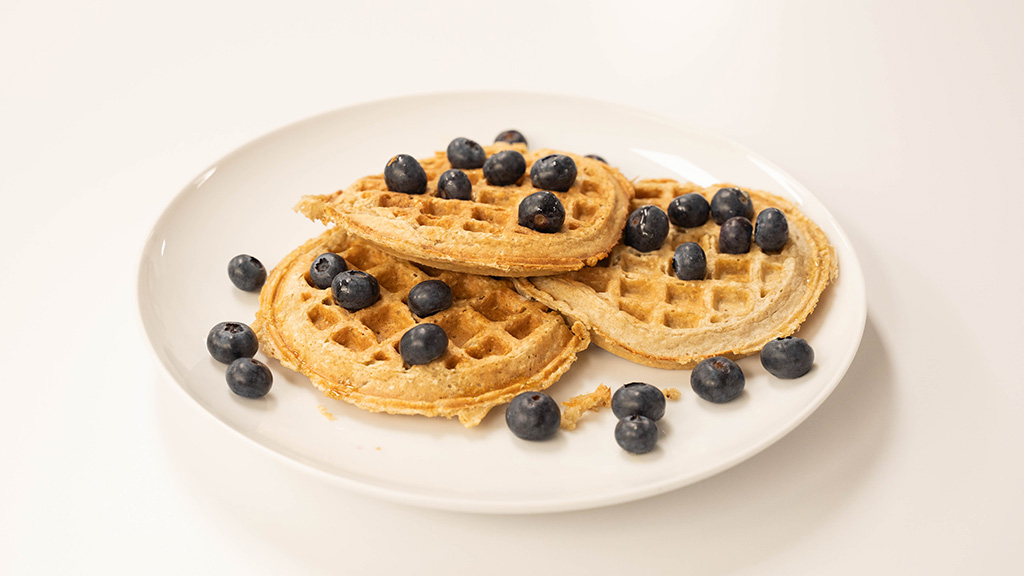 Plate of oat waffles topped with fresh blueberries.