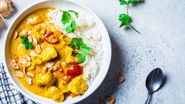 A bowl of creamy vegetable curry with rice, garnished with parsley.