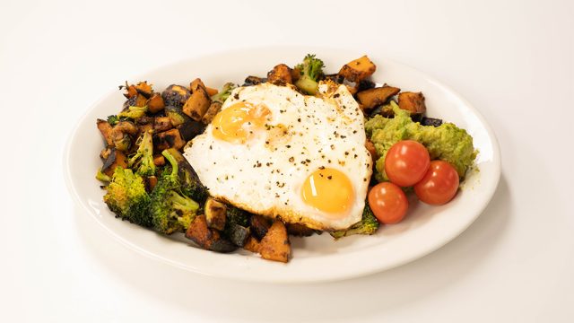 Plate of veggie hash, fried eggs, avocado, and cherry tomatoes.