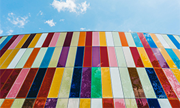 Low-angle photograph of wall made of multi-coloured panels, against blue sky